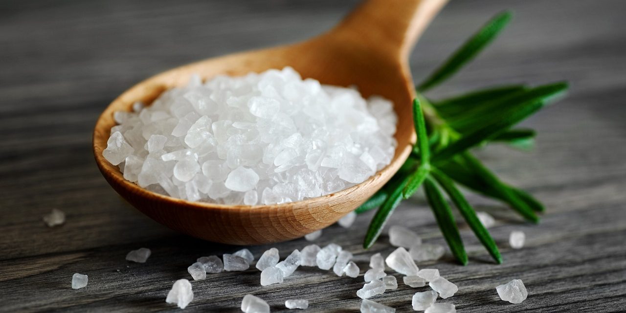 Wooden spoon with salt and rosemary on a dark background.