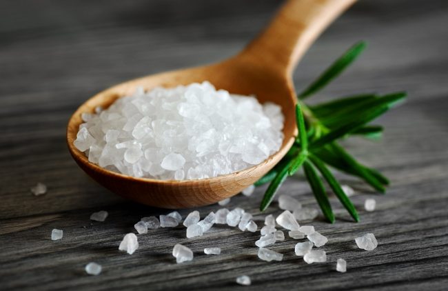 Wooden spoon with salt and rosemary on a dark background.